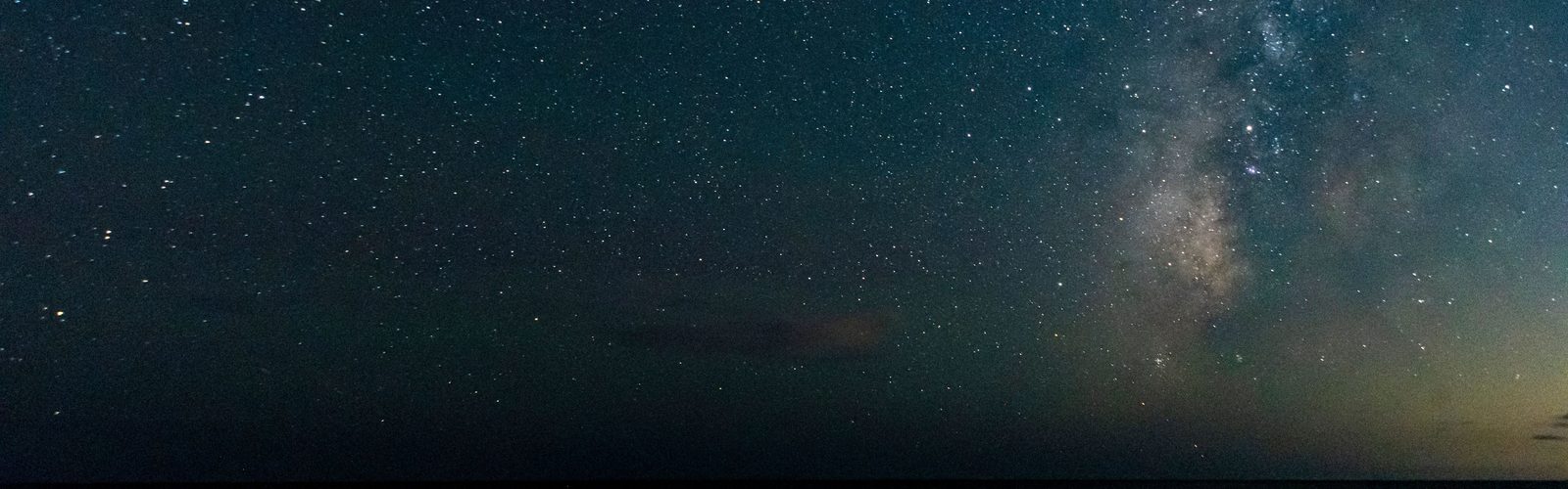 Céu noturno cheio de estrelas sobre o mar escuro, com a faixa luminosa da Via Láctea atravessando o lado direito da imagem.