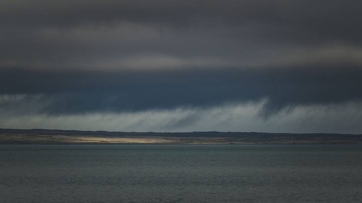 Nuvens escuras e densas de tempestade cobrindo o céu sobre o mar, com a luz baixa recortando o horizonte.