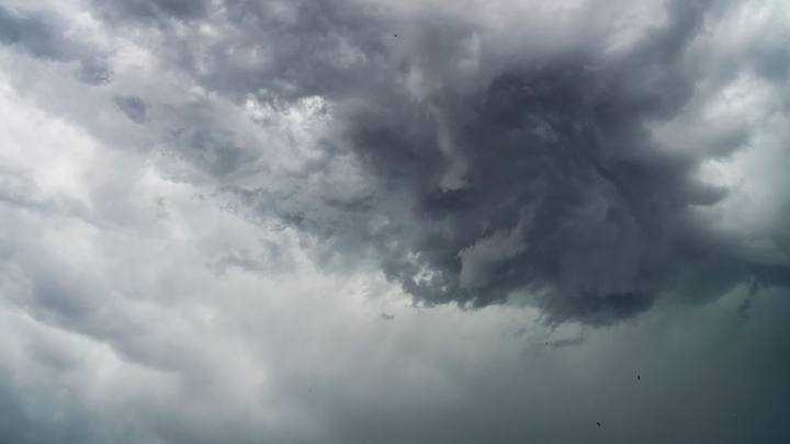 Nuvens de tempestade em movimento circular sobre o horizonte, com tons escuros e recortes de luz ao fundo.