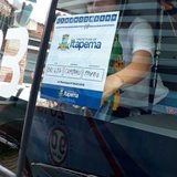Selo de papel da Prefeitura de Itapema colado por dentro no para-brisa de um ônibus de excursão, com o brasão do município, campos preenchidos à mão com a placa e a cidade de origem do veículo e a citação da lei municipal no rodapé.