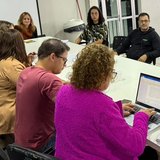 Conselheiros do conselho da criança e do adolescente de Itapema sentados em volta de uma mesa branca comprida, com um notebook aberto mostrando documento de texto e caderno de anotações sobre a mesa.