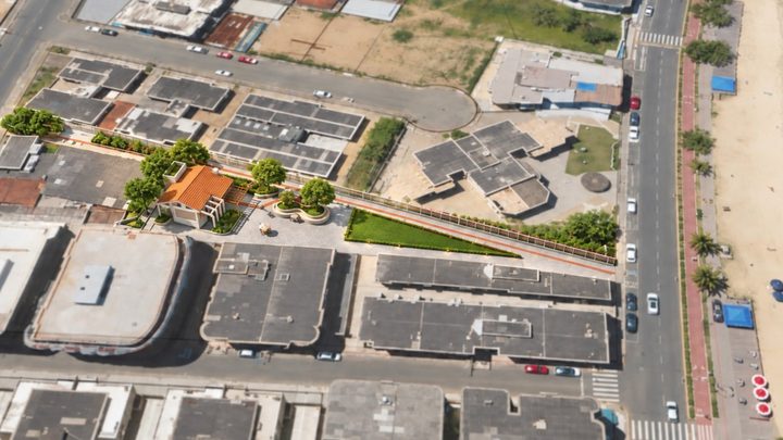 Vista aérea de um quarteirão do Centro de Itapema com o desenho do projeto da praça sobreposto à foto: um salão de telhado laranja, árvores novas, canteiro de grama e um passeio claro entre duas ruas, com a avenida da orla e a faixa de areia à direita.