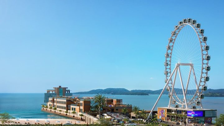 Projeção digital da orla de Itapema vista do alto, com o Píer Oporto avançando sobre o mar azul à esquerda e, à direita, uma roda-gigante branca de grande porte com cabines fechadas, montada sobre um prédio de lojas.