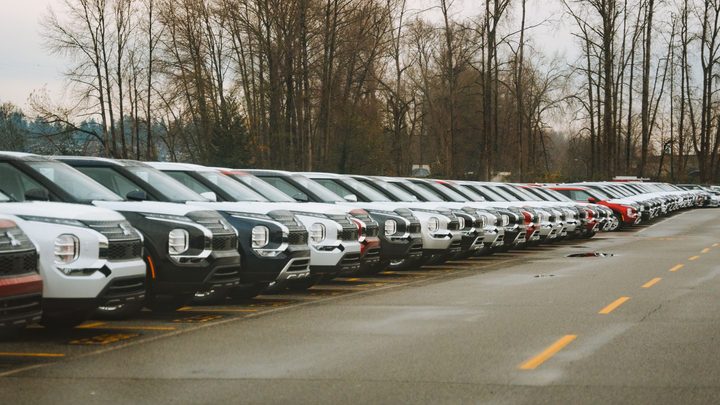 Fileira de carros novos estacionados lado a lado num pátio aberto em dia nublado, todos ainda sem placa aparente.