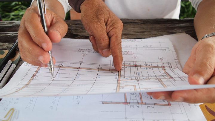 Obra viária em andamento no litoral, com máquinas trabalhando e mar ao fundo.