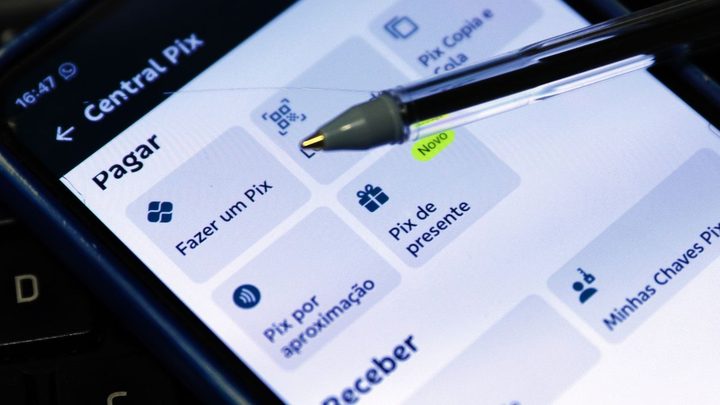 Pessoa pagando com celular por aproximação em maquininha, em balcão de comércio.
