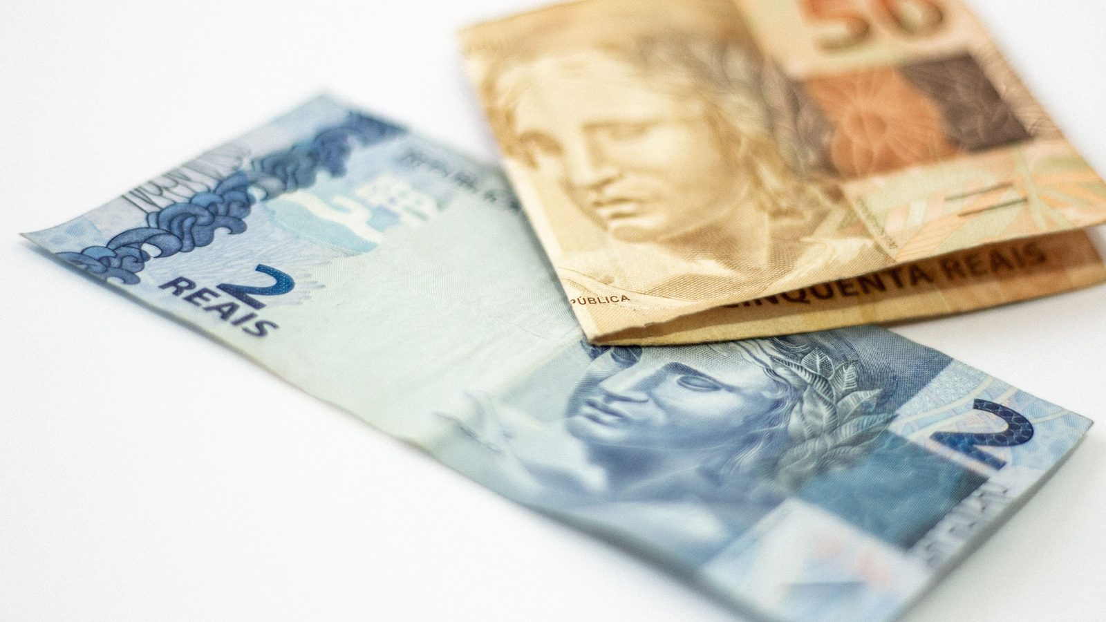 Cédulas de dois e cinquenta reais sobre fundo claro, vistas de perto.