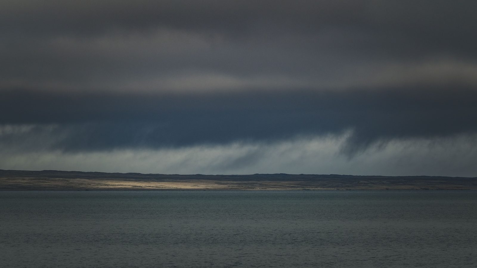 Nuvens escuras e densas de tempestade cobrindo o céu sobre o mar, com a luz baixa recortando o horizonte.